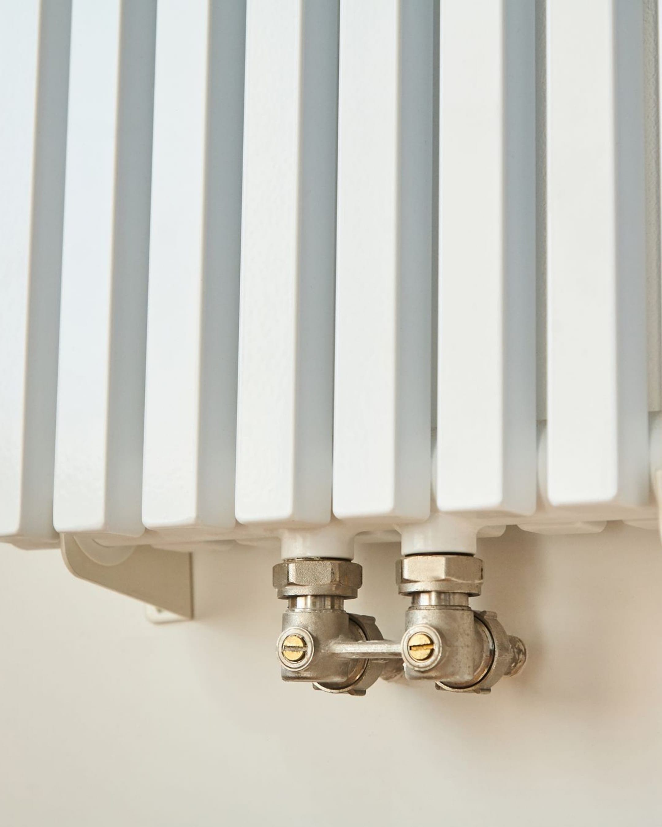 Gros plan sur un radiateur à lames verticales et ses raccords chromés.