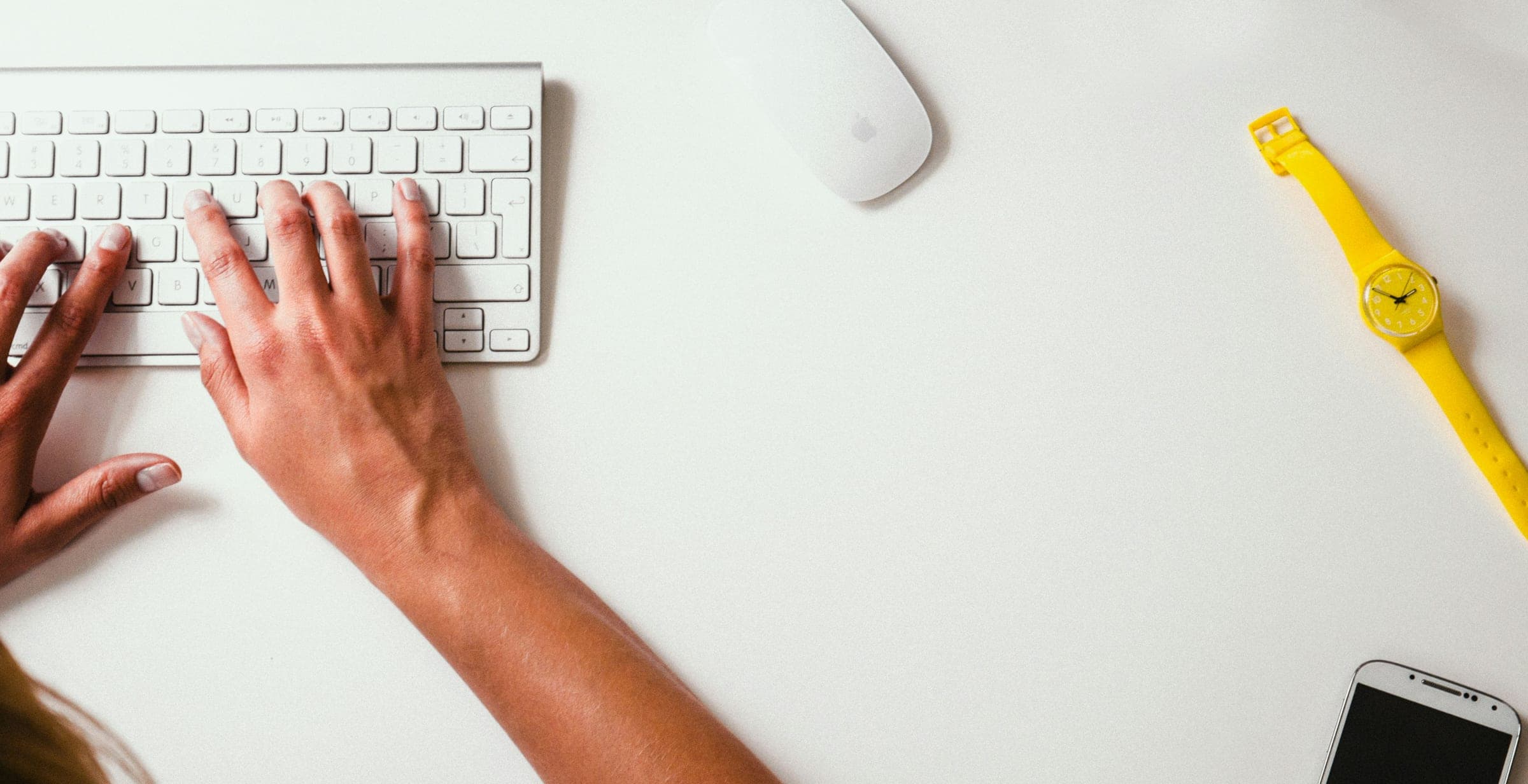 Vue en plongée d'un bureau de travail : mains en train de saisir un message au clavier d'ordinateur, montre posée à côté — illustration de la prise de contact écrite avec Victeon.