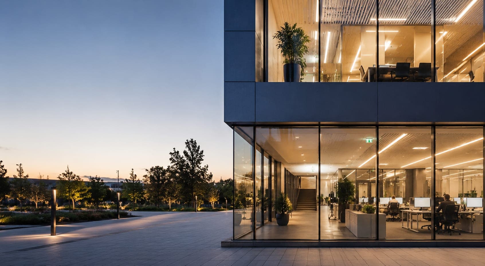 Bâtiment tertiaire moderne vu de l'extérieur au crépuscule, bureaux éclairés visibles à travers les vitres — environnement typique d'une intervention Victeon.